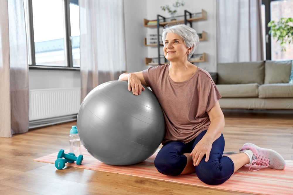 sport, fitness and healthy lifestyle concept - smiling senior woman with exercise ball sitting on mat at home. smiling senior woman with exercise ball at home