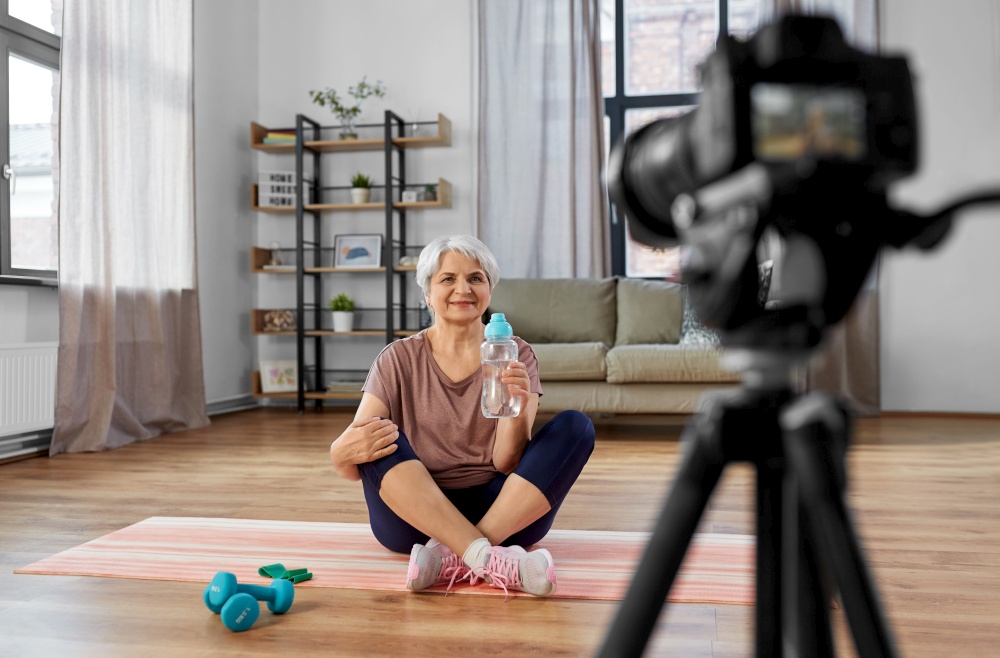 fitness, sport and video blogging concept - happy senior woman or blogger with camera streaming online class at home. woman or fitness blogger with camera at home