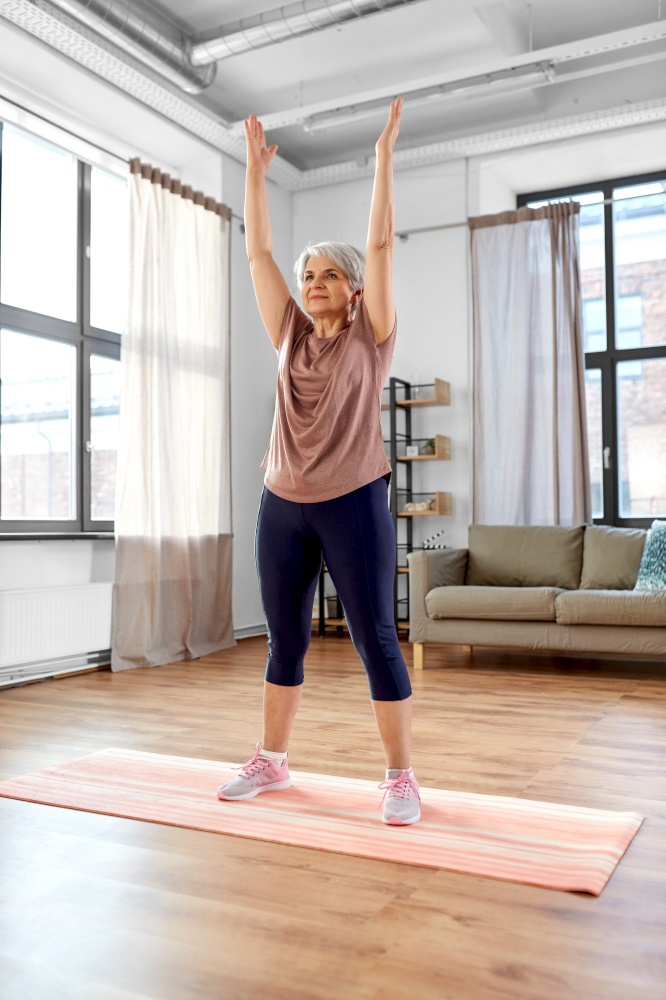 sport, fitness and healthy lifestyle concept - smiling senior woman exercising on mat at home. smiling senior woman exercising on mat at home