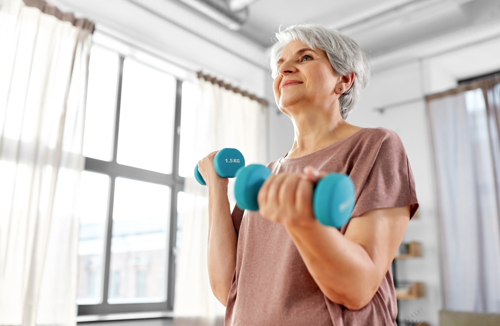 sport, fitness and healthy lifestyle concept - smiling senior woman with dumbbells exercising at home. senior woman with dumbbells exercising at home