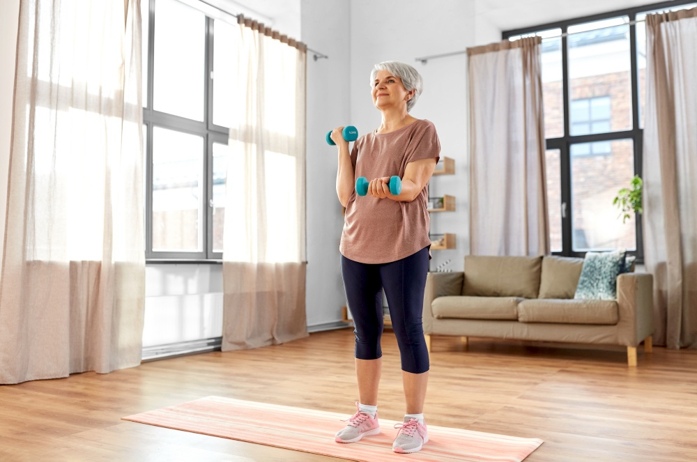 sport, fitness and healthy lifestyle concept - smiling senior woman with dumbbells exercising on mat at home. senior woman with dumbbells exercising at home