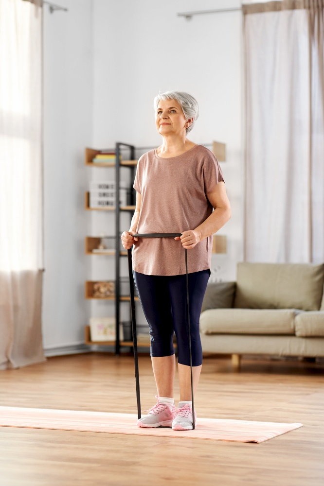sport, fitness and healthy lifestyle concept - smiling senior woman exercising with resistance band on mat at home. senior woman exercising with elastic band at home