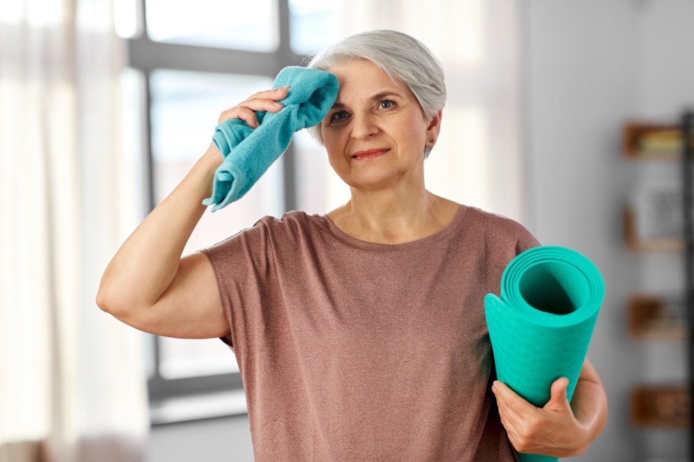 sport, fitness and healthy lifestyle concept - happy tired senior woman with yoga mat and towel at home. happy tired senior woman with yoga mat and towel