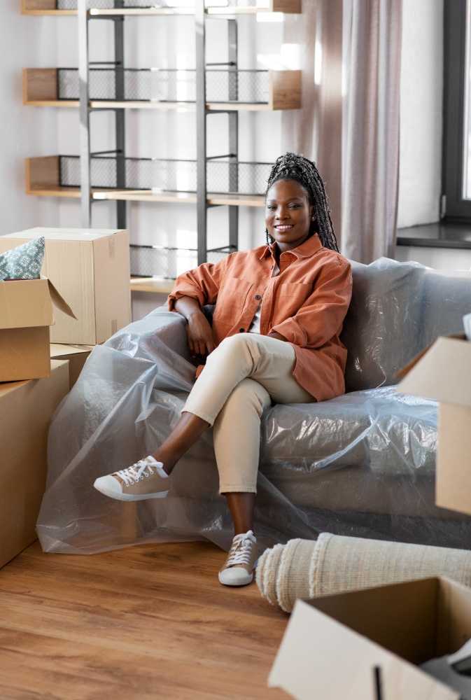 moving, people and real estate concept - happy smiling woman with boxes sitting on sofa at new home. happy woman with boxes moving to new home