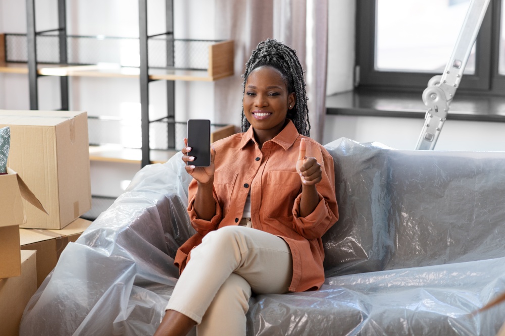 moving, repair and real estate concept - woman with smartphone and boxes showing thumbs up at new home. woman with phone moving home and showing thumbs up