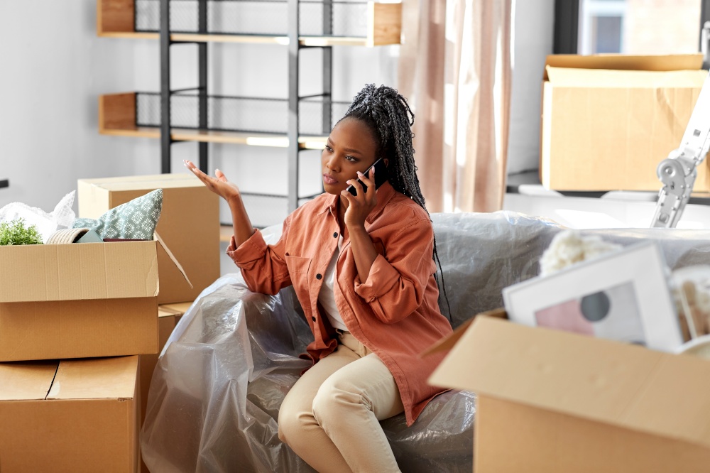 moving, people and real estate concept - angry woman with boxes calling on smartphone at new home. woman calling on phone moving to new home