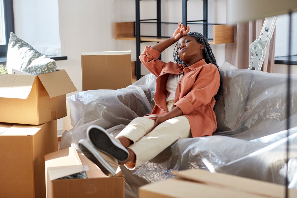 moving, people and real estate concept - tired woman with boxes resting on sofa at new home. tired woman resting while moving to new home