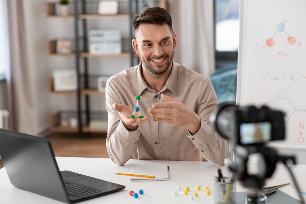 distance education, school and video blogging concept - happy smiling male chemistry teacher with camera and molecule model having online class at home office. chemistry teacher with camera having online class