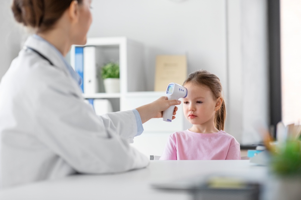medicine, healthcare and pediatry concept - female doctor or pediatrician measuring little girl patient&rsquo;s temperature with infrared forehead thermometer at clinic. female doctor and little girl patient at clinic