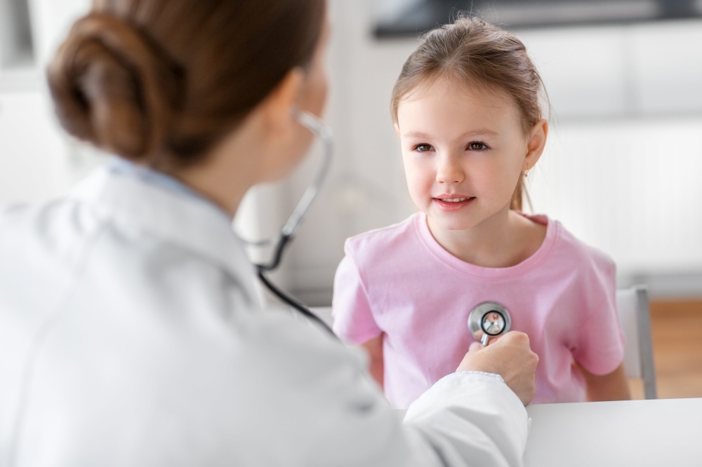 medicine, healthcare and pediatry concept - female doctor or pediatrician with stethoscope and little girl patient on medical exam at clinic. doctor with stethoscope and girl patient at clinic