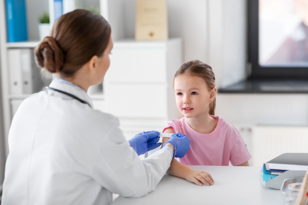 medicine, healthcare and vaccination concept - female doctor or pediatrician talking to little girl patient on medical exam at clinic. female doctor and little girl patient at clinic