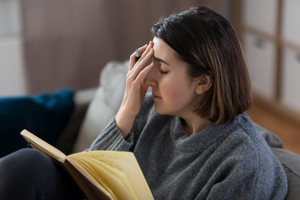 stress, mental health and depression concept - stressed unhappy woman with diary sitting on sofa at home. sad woman with diary sitting on sofa at home