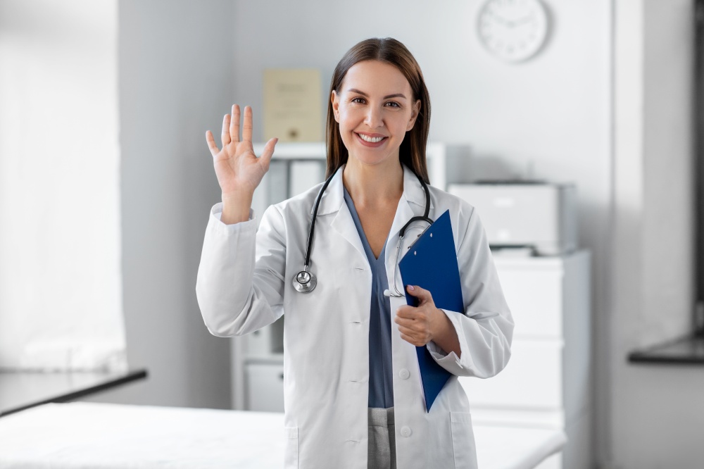 medicine, healthcare and profession concept - smiling female doctor with stethoscope and clipboard waving hand at hospital. smiling female doctor with clipboard at hospital