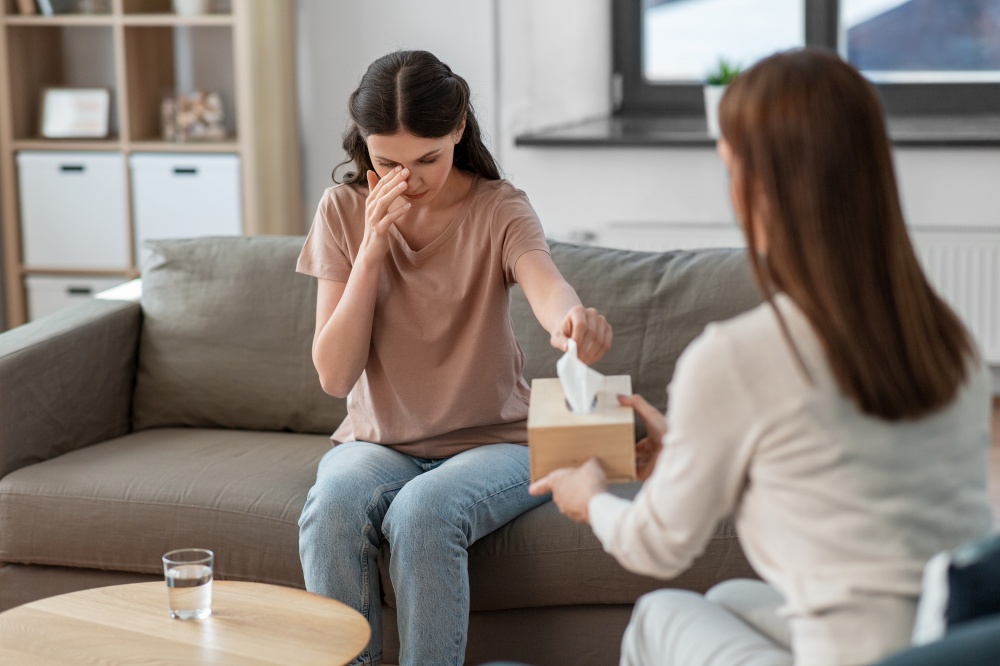 psychology, mental health and people concept - crying woman patient taking paper tissue from psychologist at psychotherapy session. crying woman and psychologist at psychotherapy
