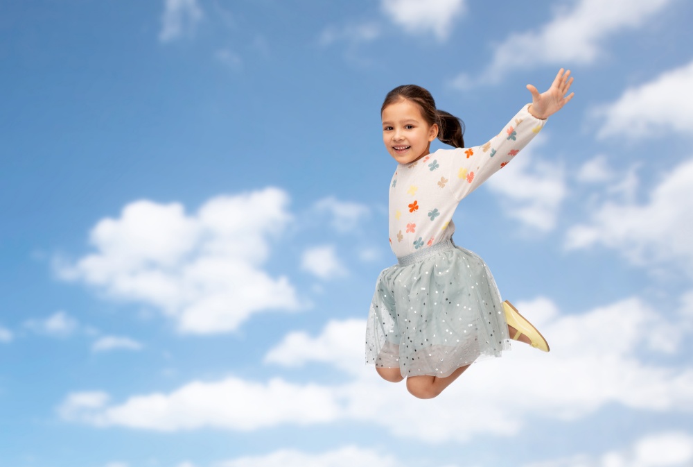 birthday, childhood and people concept - happy smiling little girl jumping over blue sky and clouds background. happy little girl jumping over blue sky and clouds