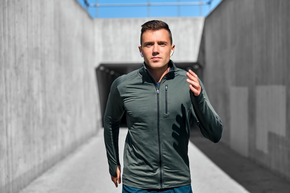 fitness, sport, training and lifestyle concept - young man with wireless earphones running outdoors. young man with wireless earphones outdoors