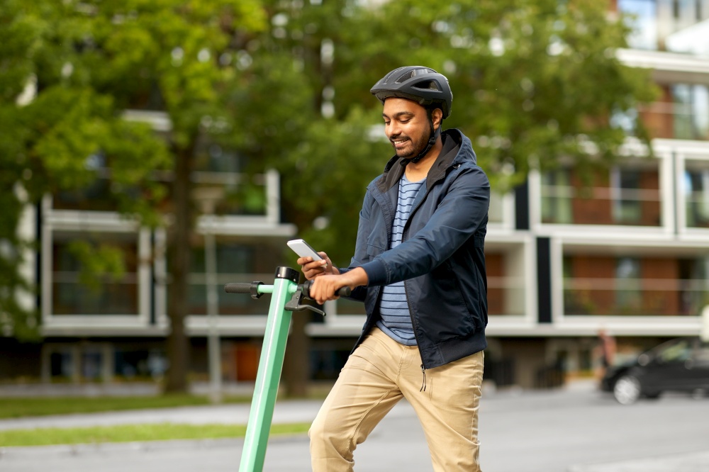 transport, technology and people and concept - happy smiling young man in helmet with electric scooter using smartphone on city street. man with smartphone and electric scooter in city