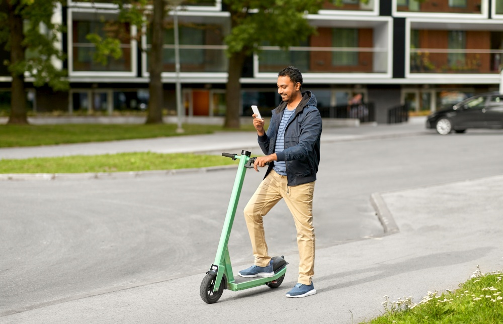 transport, technology and people and concept - happy smiling young man with electric scooter using smartphone on city street. man with smartphone and electric scooter in city