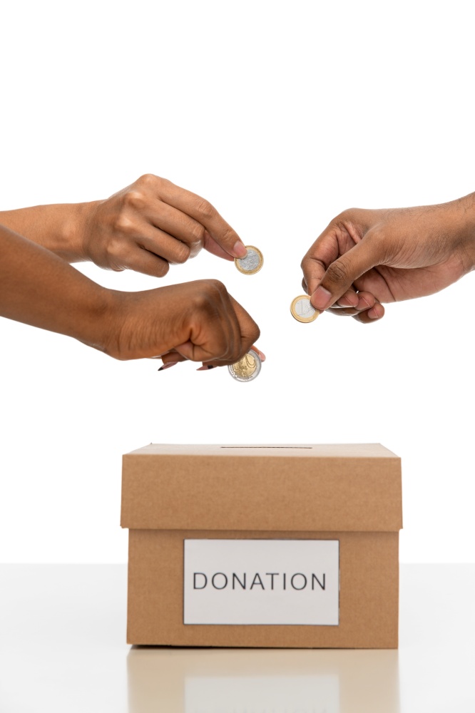 charity, financial support and saving concept - close up of hands putting coins into donation box. close up of hands putting coins into donation box
