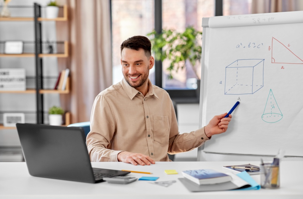 distant education, school and remote job concept - happy smiling male math teacher with laptop compute showing geometric shapes on flip chart having online class or video call at home office. math teacher with laptop has online class at home
