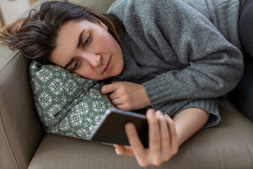 mental health, psychological help and depression concept - stressed woman with smartphone lying on sofa at home. stressed woman with smartphone on sofa at home