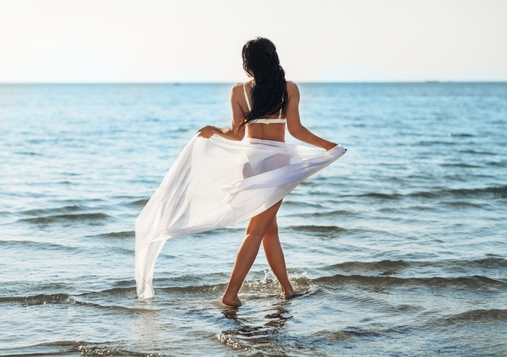people, summer and swimwear concept - woman in bikini swimsuit with pareo on beach. woman in bikini swimsuit with pareo on beach