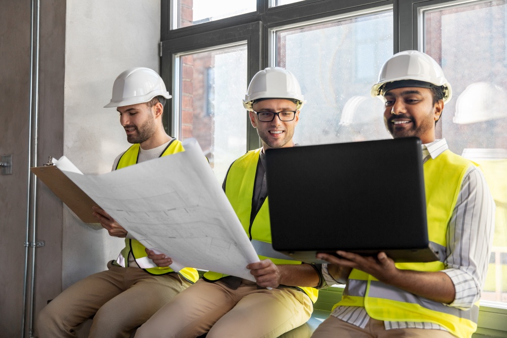architecture, construction business and people concept - male architects in helmets with laptop, blueprint and clipboard working at office. male architects in helmets with laptop at office