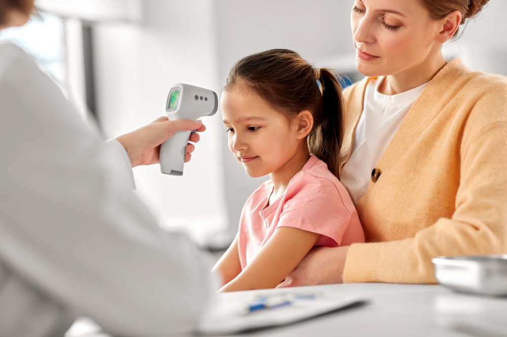 medicine, healthcare and pediatry concept - mother with sick little daughter and doctor measuring temperature with infrared forehead thermometer at clinic. mother with sick daughter and doctor at clinic