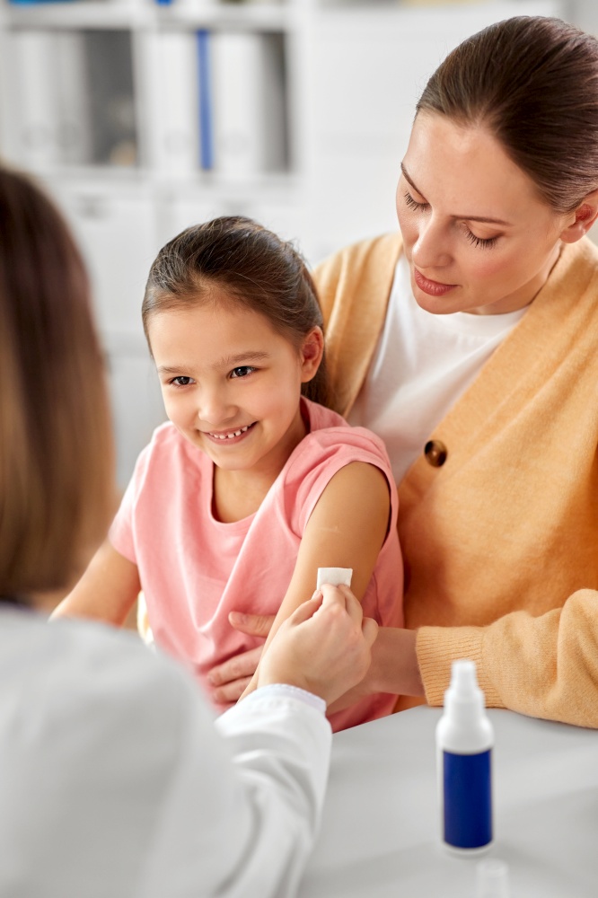 medicine, healthcare and pediatry concept - female doctor or pediatrician disinfecting arm skin of little girl patient with mother at clinic. doctor preparing child for vaccination at clinic