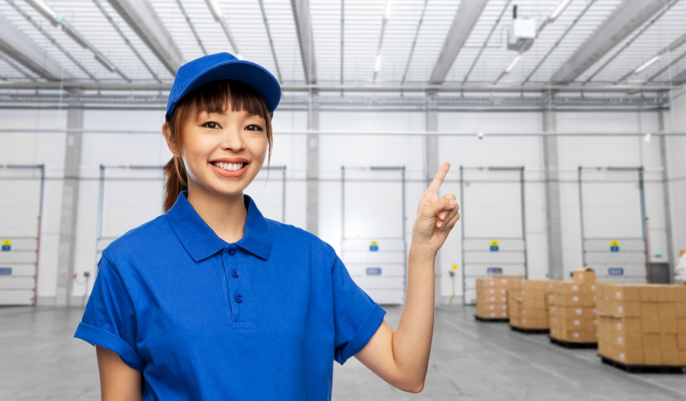 profession, job and people concept - happy smiling delivery woman in blue uniform over warehouse background. happy smiling delivery woman over warehouse