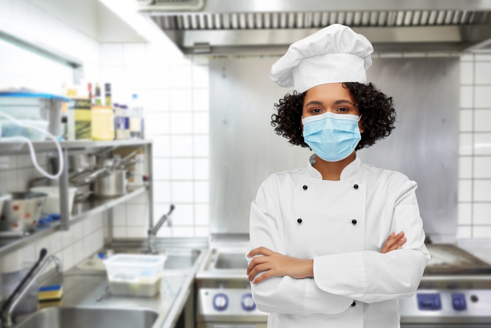 cooking, pandemic and health concept - happy smiling female chef in protective medical mask over restaurant kitchen background. female chef in medical mask and toque