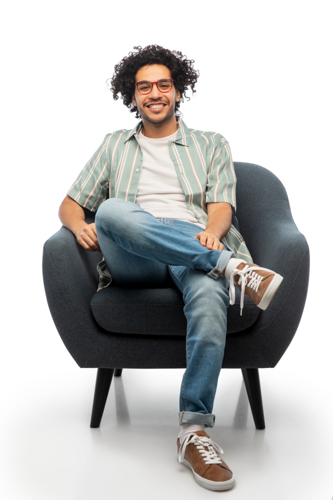 people and furniture concept - happy smiling young man in glasses sitting in chair over white background. happy smiling young man sitting in chair