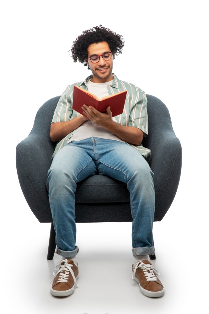 people and furniture concept - happy smiling young man in glasses reading book sitting in chair over white background. happy smiling man reading book sitting in chair