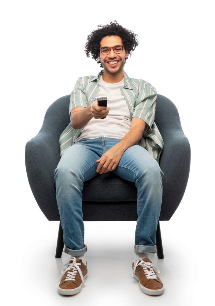 leisure, people and furniture concept - happy smiling young man in glasses tv remote control sitting in chair over white background. happy man with tv remote control sitting in chair