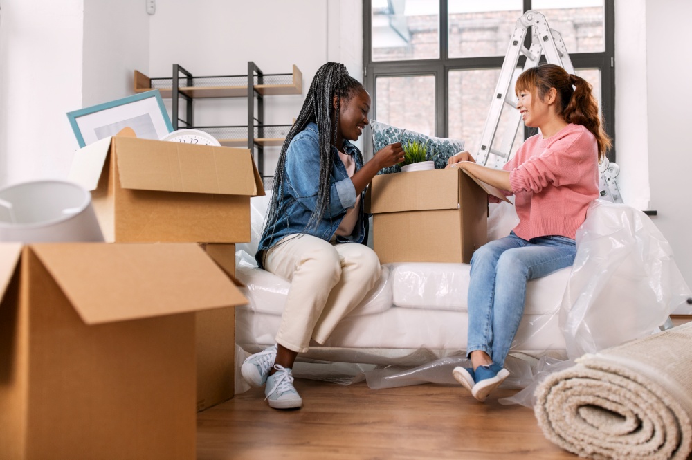 moving, people and real estate concept - happy smiling women unpacking boxes at new home. women unpacking boxes and moving to new home
