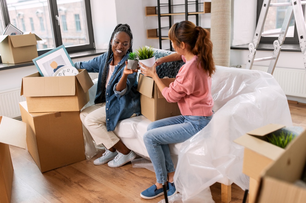 moving, people and real estate concept - happy smiling women unpacking boxes at new home. women unpacking boxes and moving to new home