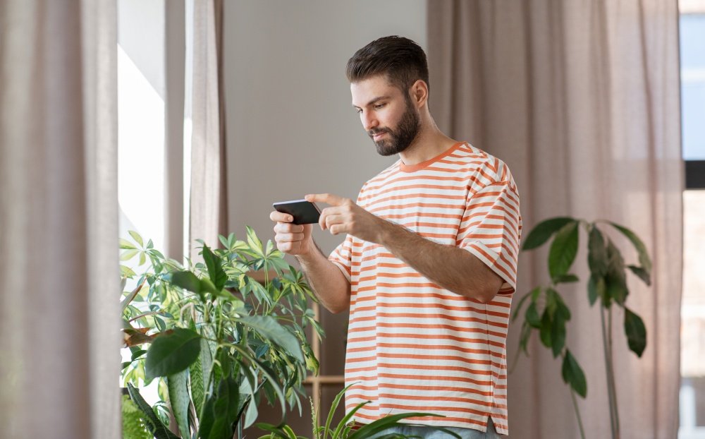 technology, people and internet concept - happy smiling man with smartphone and flowers at home. man with smartphone and flowers at home