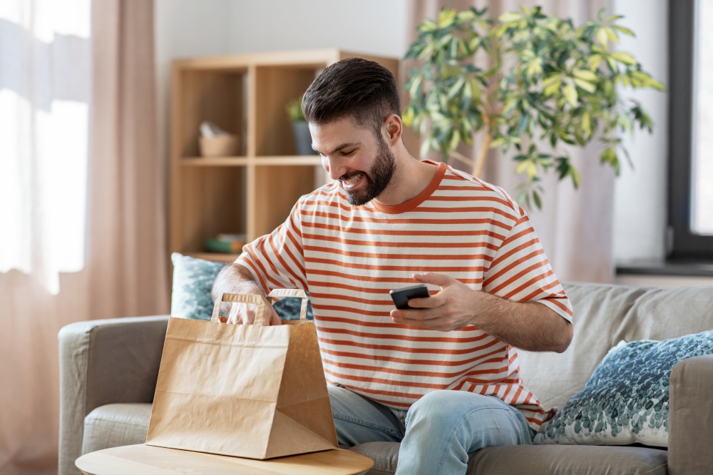 communication, leisure and people concept - happy smiling man using smartphone for takeaway food order check up at home. man with phone checking food order at home