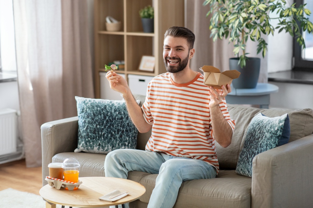 consumption, delivery and people concept - smiling man with fork eating takeaway food at home. smiling man eating takeaway food at home