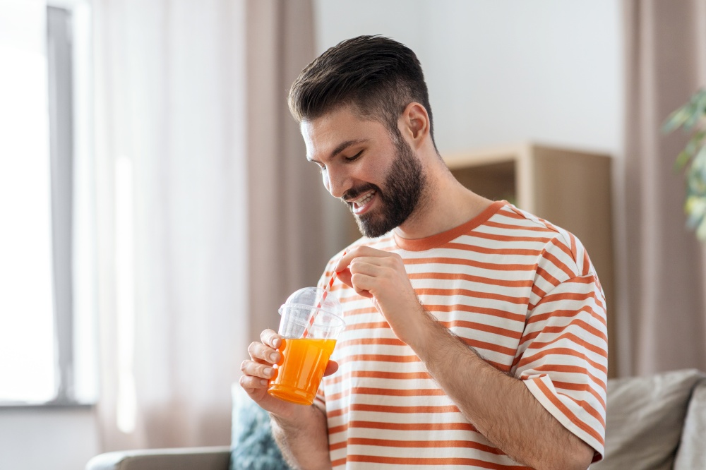 drinks and people concept - smiling man drinking orange juice with straw at home. smiling man drinking orange juice at home