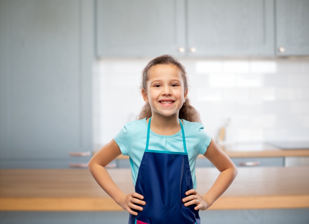cooking, culinary and profession concept - happy smiling little girl in apron over home kitchen background. smiling little girl in apron over home kitchen