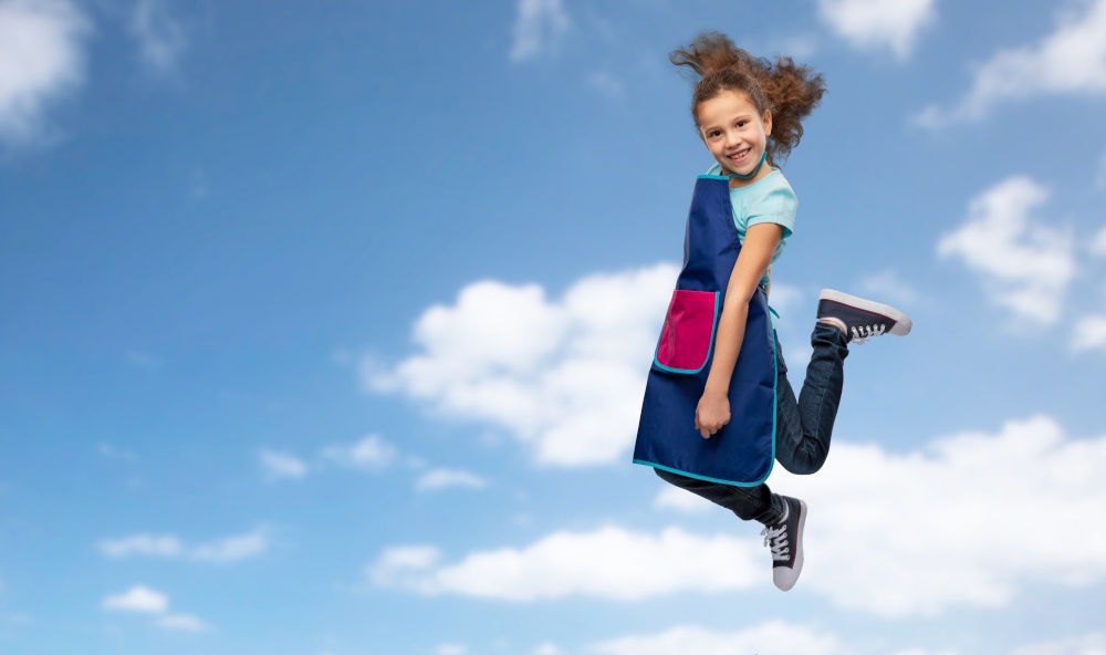 cooking, culinary and profession concept - happy smiling little girl in apron jumping over blue sky and clouds background. smiling little girl in apron jumping in sky