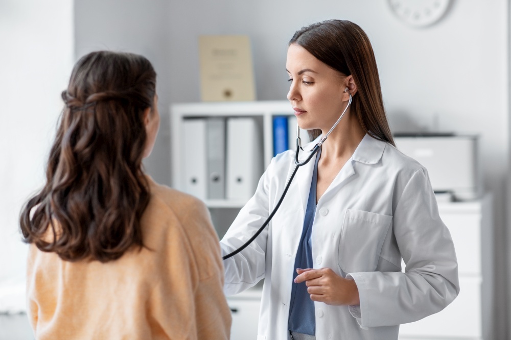 medicine, healthcare and people concept - female doctor with stethoscope listening to woman patient at hospital. doctor with stethoscope and woman at hospital