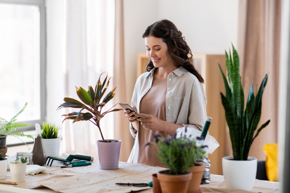 people, gardening and housework concept - happy woman with smartphone and pot flower at home. woman with smartphone and pot flower at home