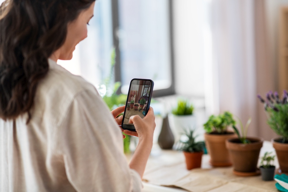 people, gardening and housework concept - happy woman with smartphone photographing pot flowers at home. woman with smartphone photographing pot flowers