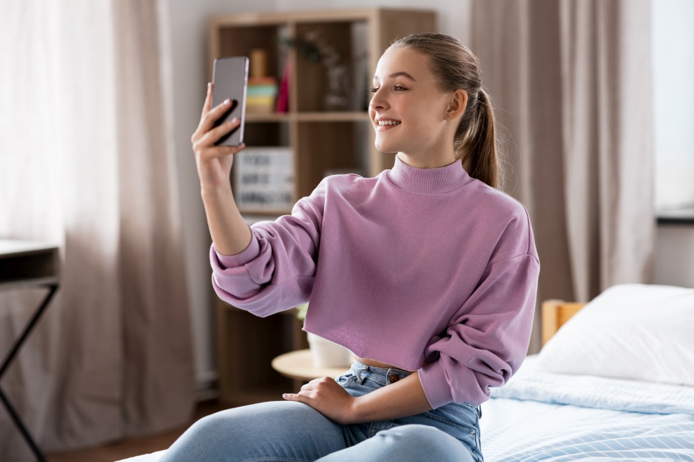 people, children and technology concept - happy smiling teenage girl with smartphone taking selfie at home. happy girl with smartphone taking selfie at home