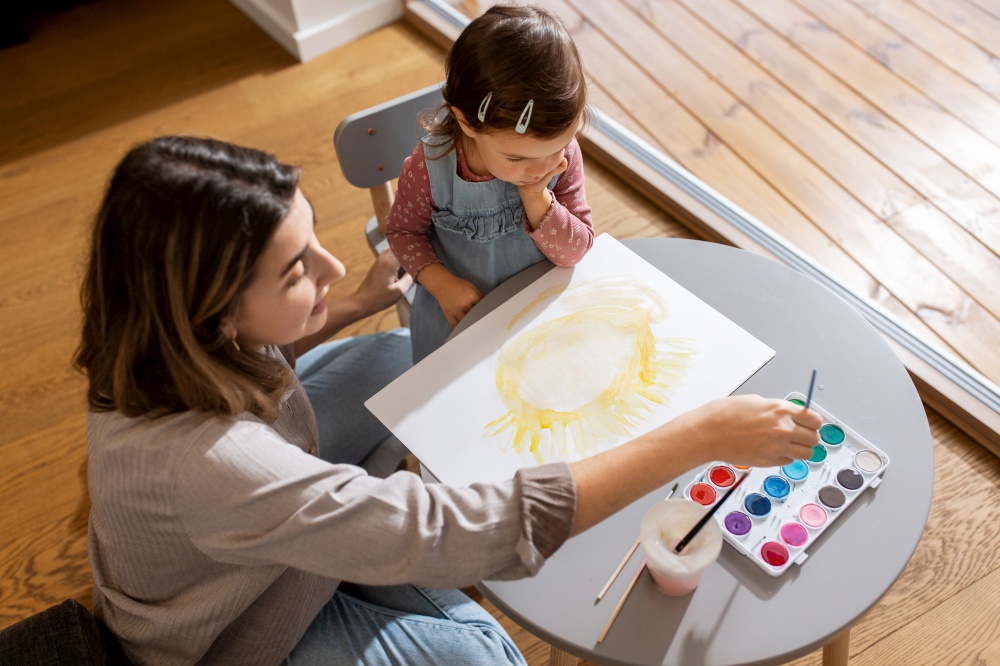 family, motherhood and leisure concept - mother spending time with her little daughter and drawing sun at home. mother with little daughter drawing sun at home