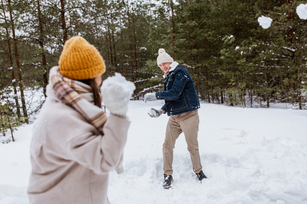 people, season and leisure concept - happy couple playing snowballs in winter park. happy couple playing snowballs in winter park