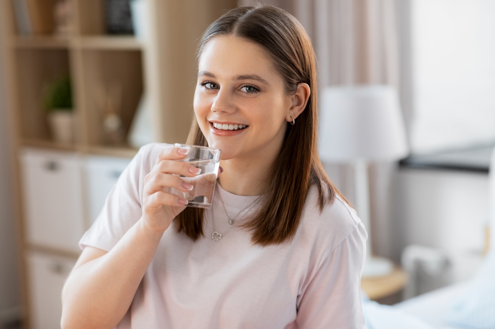 health and people concept - happy smiling girl with glass drinking water at home. smiling girl with glass drinking water at home
