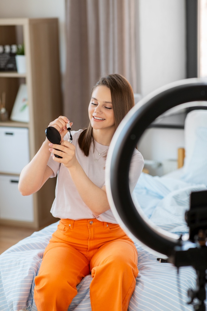 beauty blogging, make up and people concept - happy smiling girl blogger with ring light and smartphone applying mascara at home. girl blogger with ring light applying make up